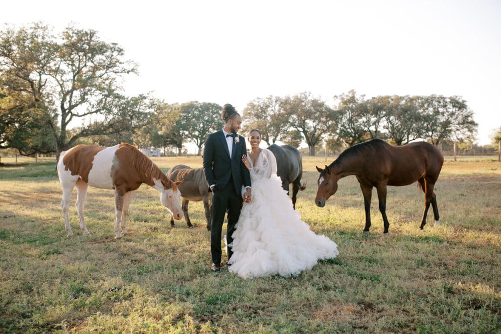 black groom and black bride stand side by side in field of horses in Austin wedding venue