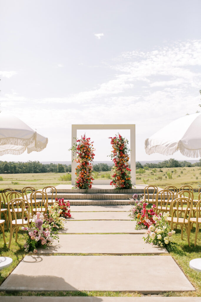 Ceremony arch with bright flowers and white umbrellas in grassy field at Prospect House